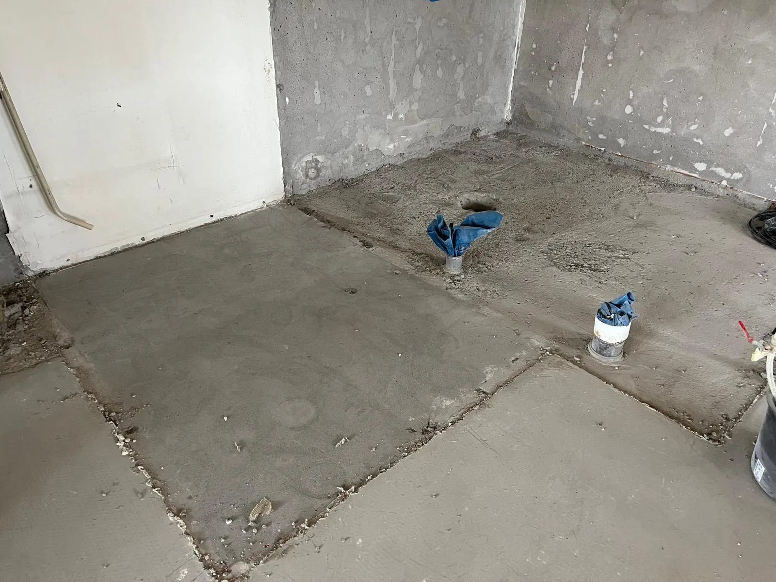 Huoneen lattia on betonia, jossa on kaksi putkea ja sininen kangas.