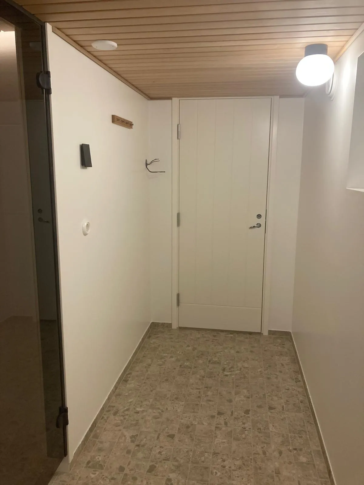 Valkoinen eteinen, puukatto, marmorilattia ja valaisin.