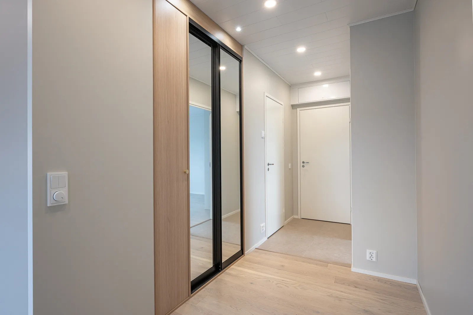 Vaaleassa huoneessa on vaatekaappi peiliovilla, valkoiset seinät ja katto sekä vaalea puulattia.