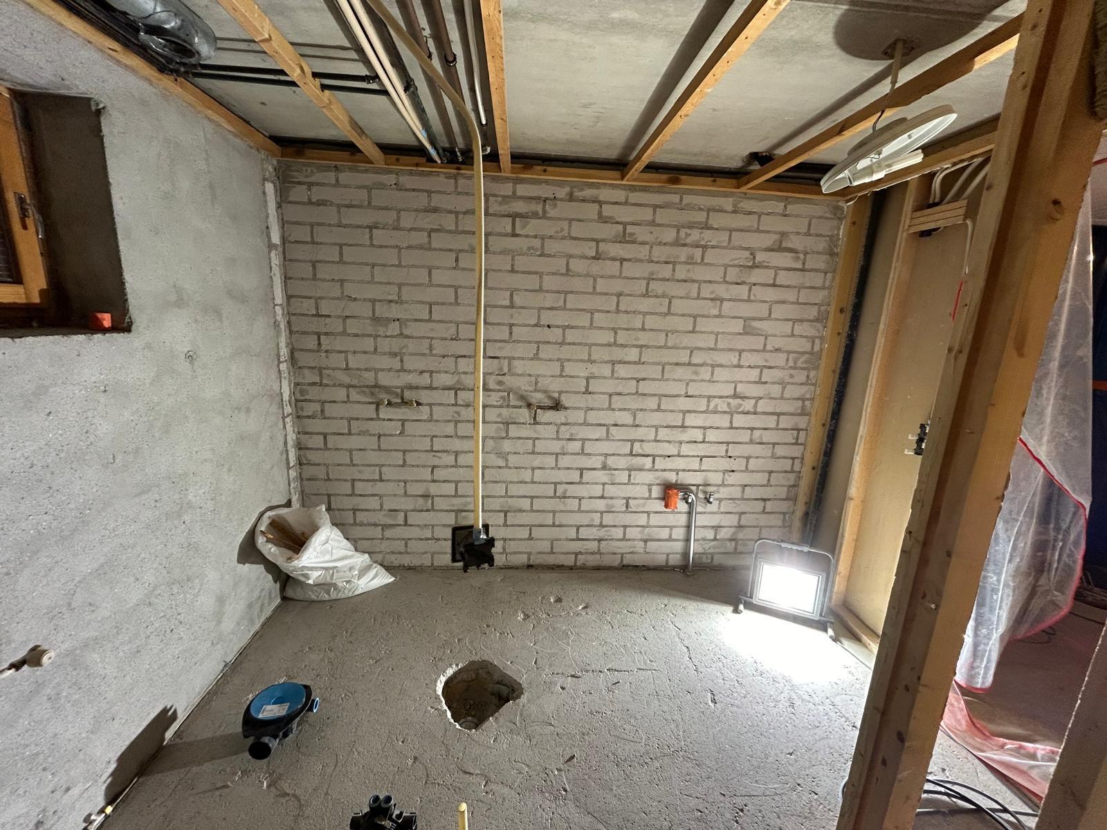 Keskeneräinen huone, jossa on betonilattia, tiiliseinä, puukatto ja työvalo.