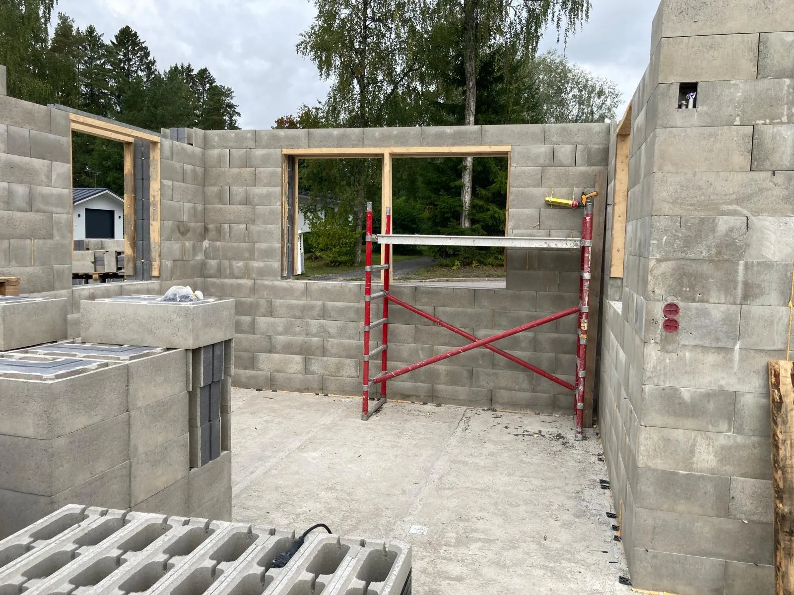 Rakenteilla oleva kivitalo, jossa on punainen rakennusteline ja harmaat betoniharkot. Valoisa sää.