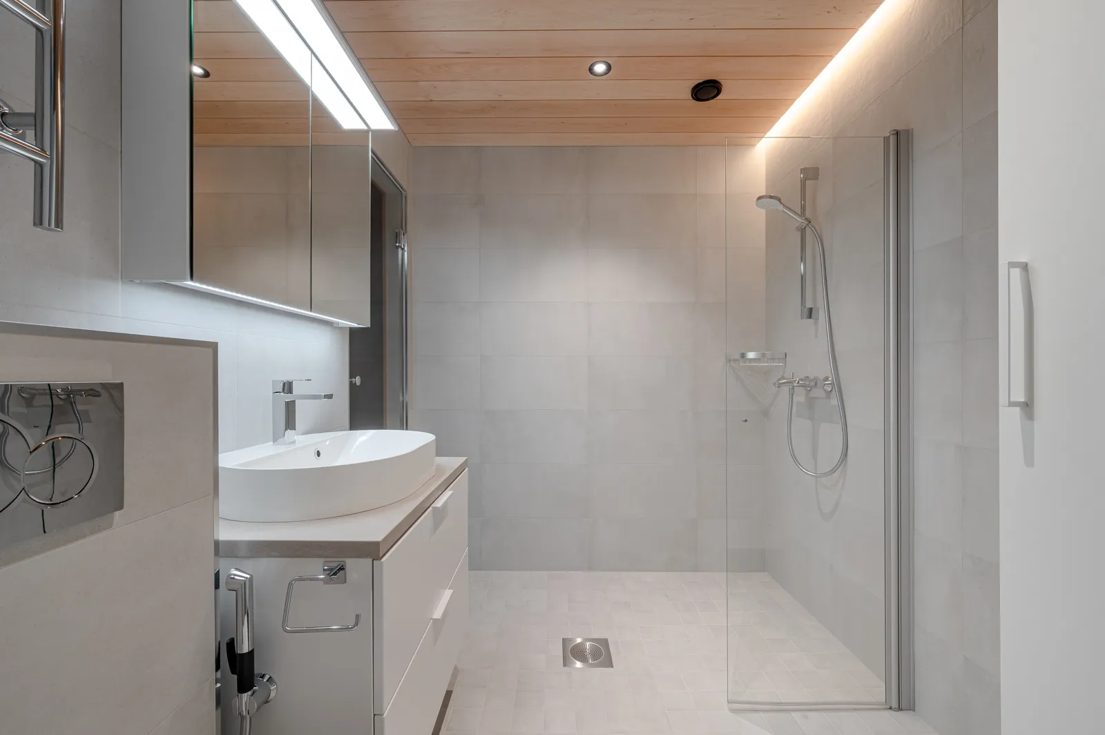 Moderni kylpyhuone, jossa on puinen katto, valkoinen pesuallas, suihku lasiovella ja harmaat laatat.