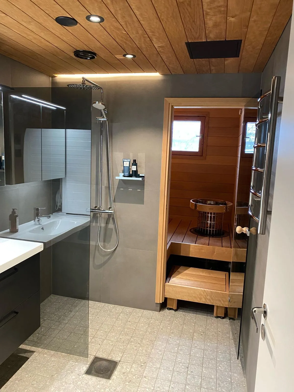 Moderni kylpyhuone, jossa on puinen sauna, harmaat laatat, puukatto ja suihku.