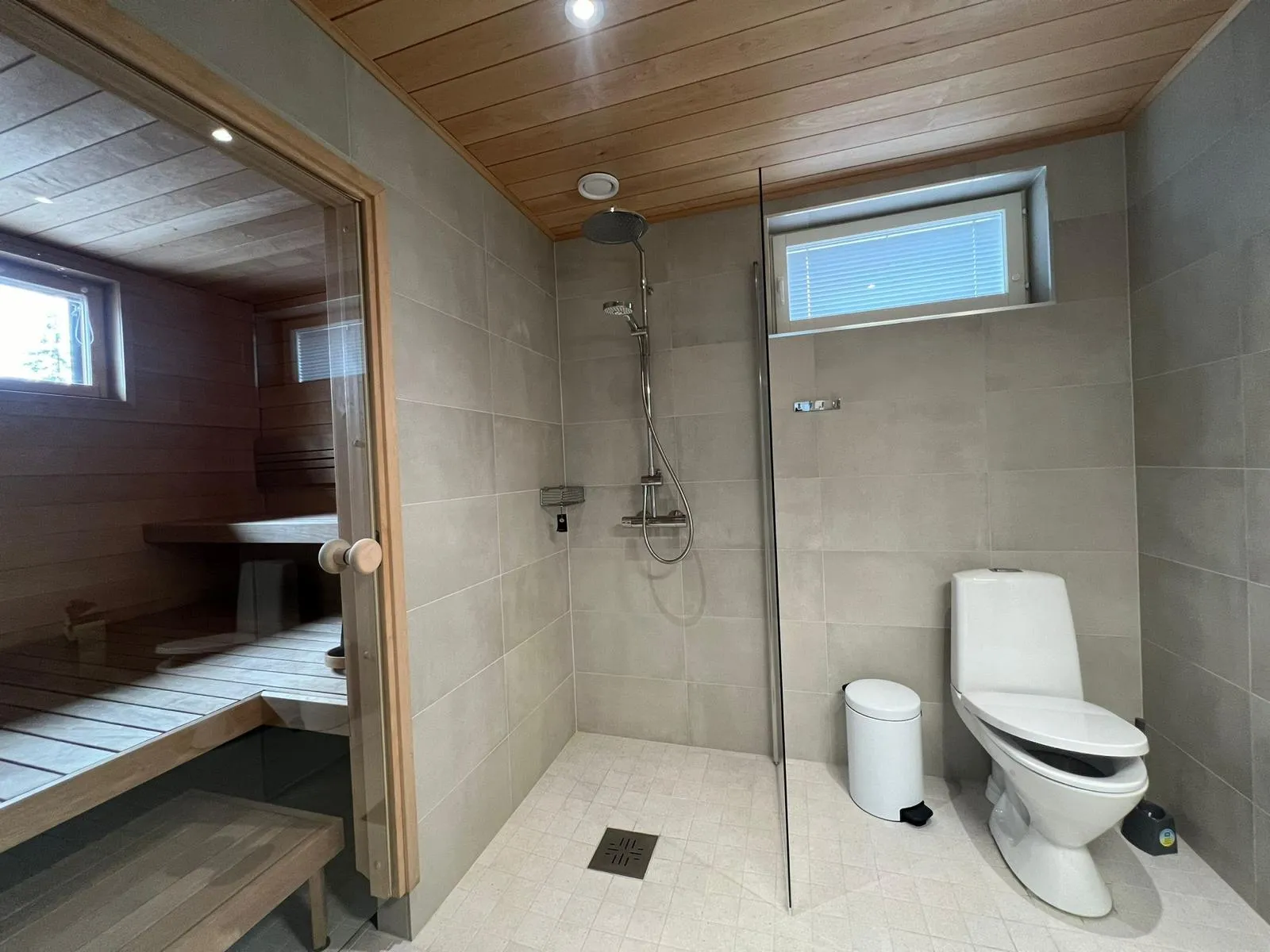 Kylpyhuoneessa on suihku, wc, roskakori ja sauna, jossa on puinen sisustus ja penkit.