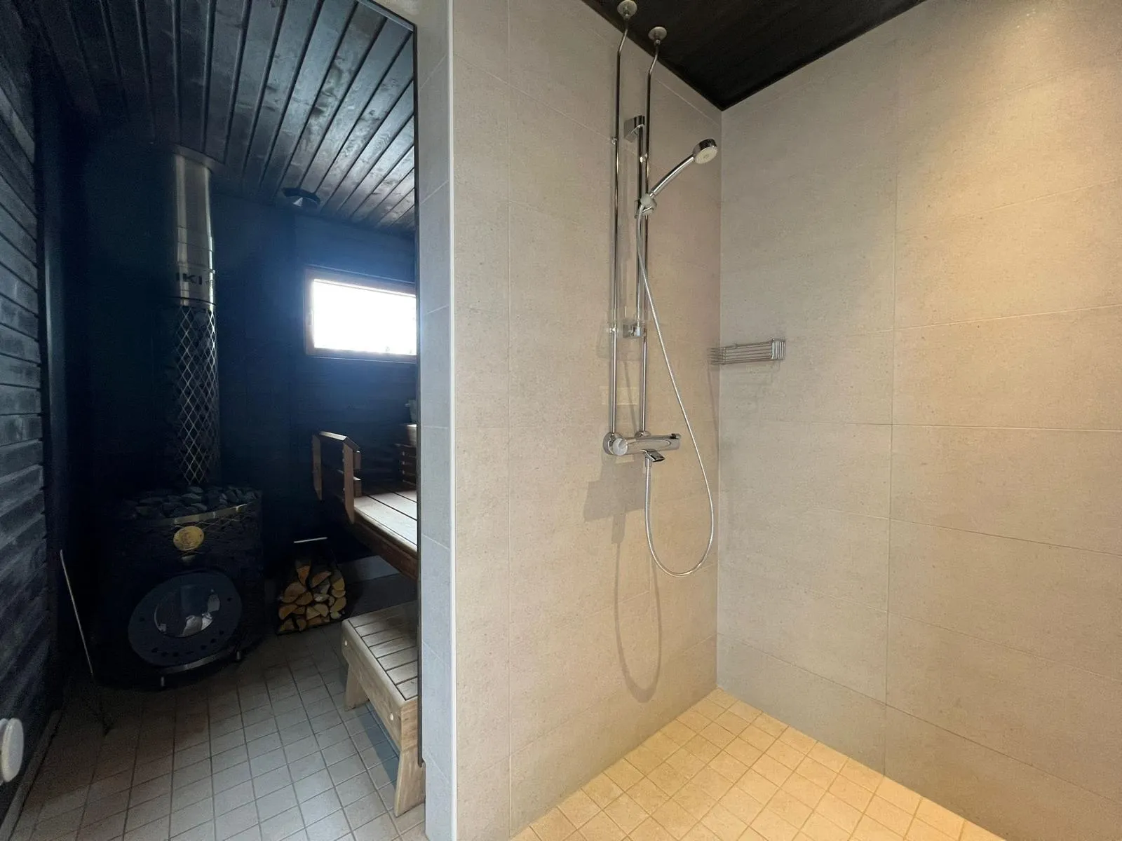 Valoisa kylpyhuone suihkulla ja saunalla, jossa on puukiuas ja lauteet.