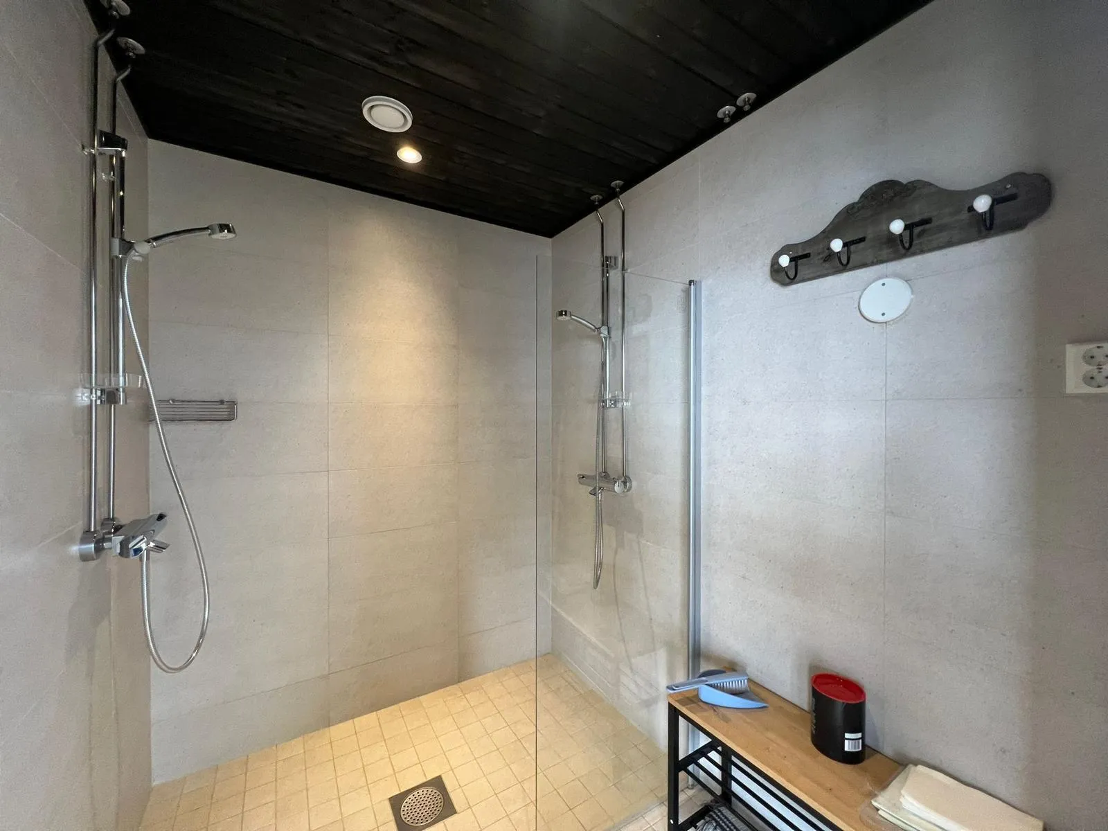 Kylpyhuoneessa on kaksi suihkua, lasiseinä, puinen katto, pyyheteline ja pieni hylly, jossa on harja, purkki ja pyyhkeitä.