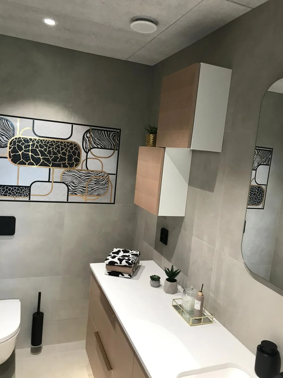 Moderni kylpyhuone, jossa on taidetta, puu-valkoiset kaapit, valkoinen työtaso ja peili.