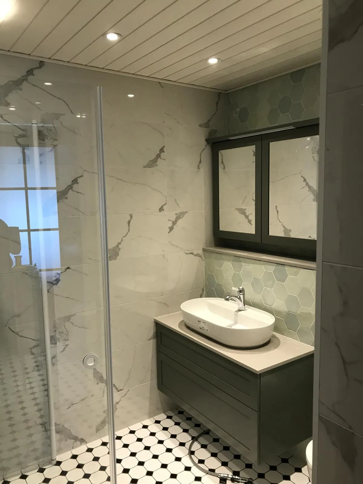 Kylpyhuoneen sisustus, jossa on marmorikuvioiset seinälaatat, valkoinen pesuallas harmaalla kaapilla ja mustavalkoinen lattia.