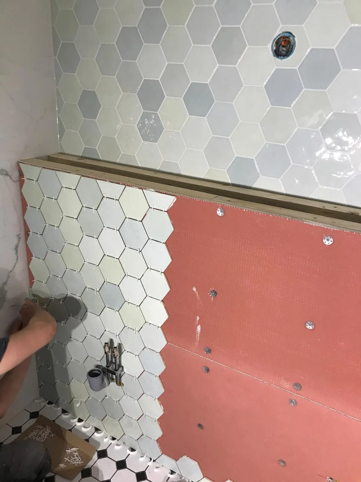 Kuusikulmaisten laattojen asennus kylpyhuoneessa, jossa näkyy oranssi taustalevy ja valkoiset saumat.