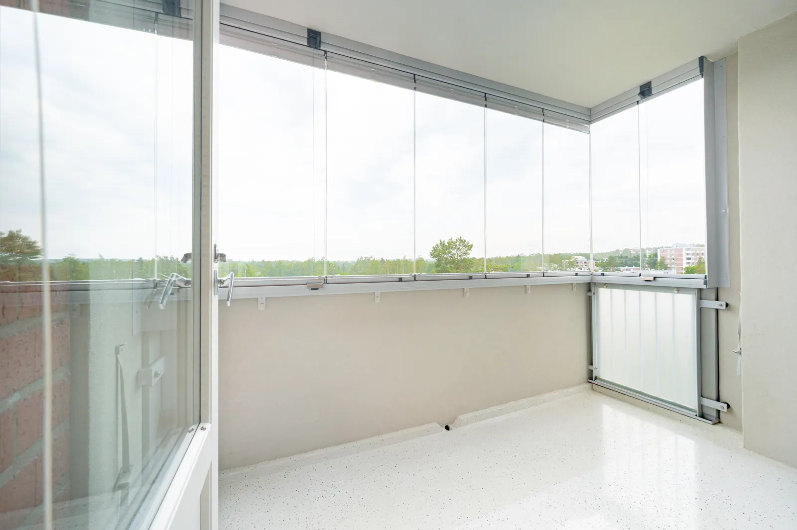 Lasitetulla parvekkeella on valkoiset seinät ja lattia, ja näkymä ulos on vihreä.