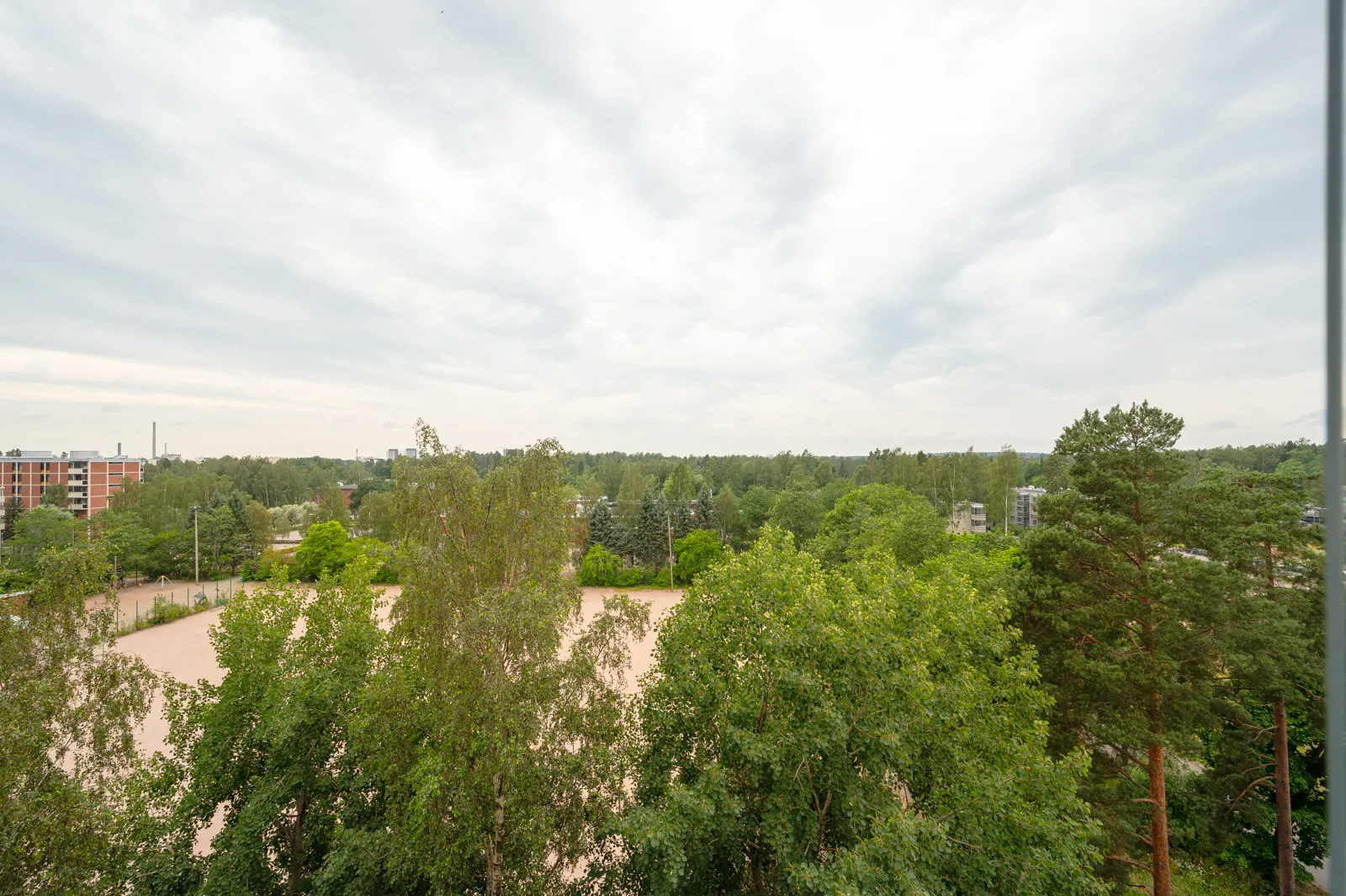 Ylänäkymä puistoon, jossa on ruskea kenttä, rakennuksia ja pilvinen taivas.