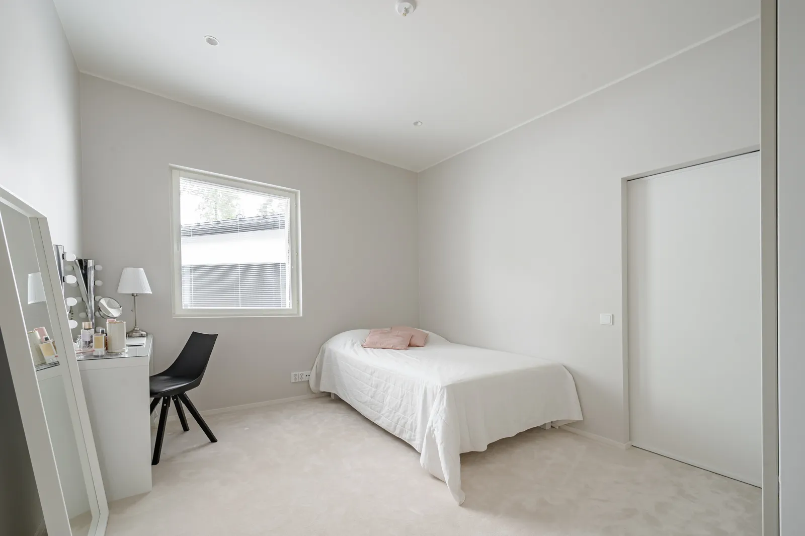 Vaaleassa makuuhuoneessa on sänky, peilipöytä ja musta tuoli. Huoneessa on valoisa tunnelma ja minimalistinen sisustus.