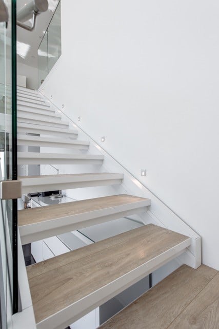 Modernit portaat vaalealla puulla ja valkoisella rungolla, lasikaide ja seinään upotetut valot.