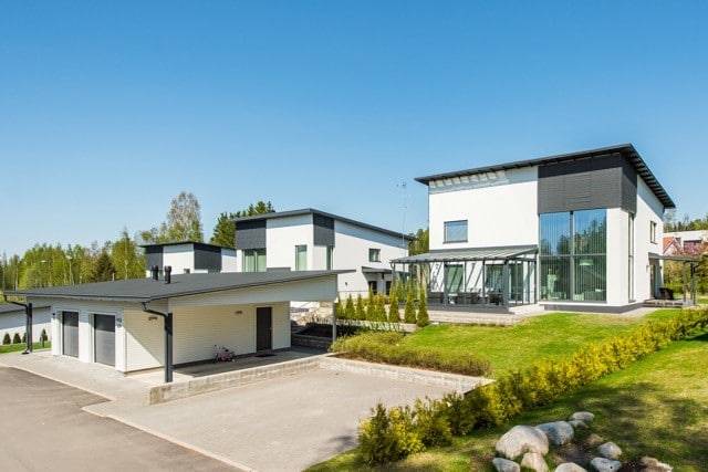 Kolme modernia valkoista taloa, joissa on tummat katot ja suuret ikkunat, aurinkoisena päivänä.