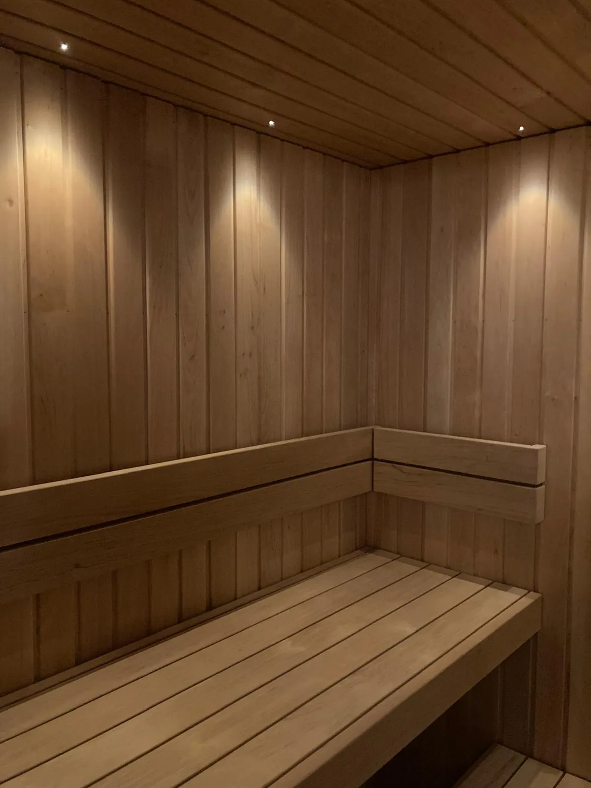 Puinen sauna, jossa on penkki, puupaneelit ja epäsuora valaistus.