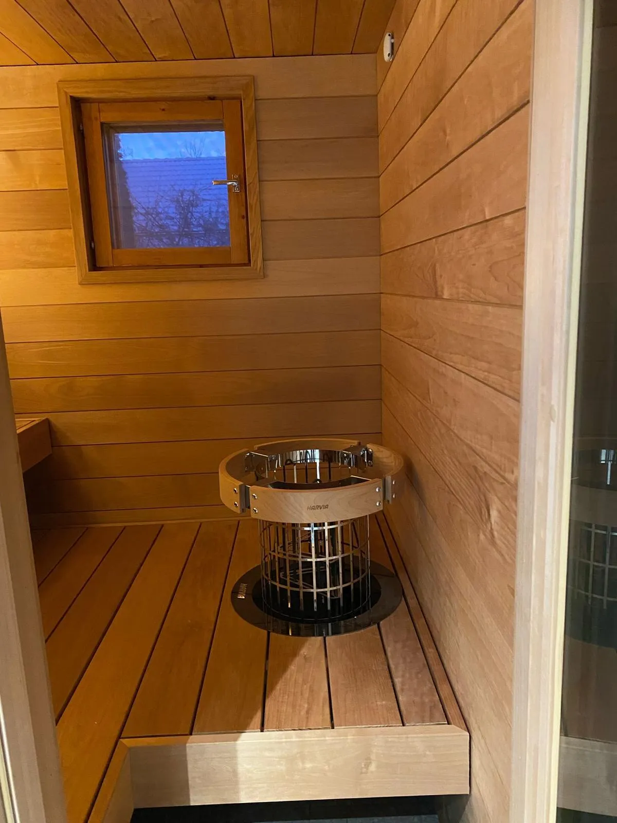 Puinen sauna, jossa on ikkuna, Harvia-kiuas ja puupaneelit.