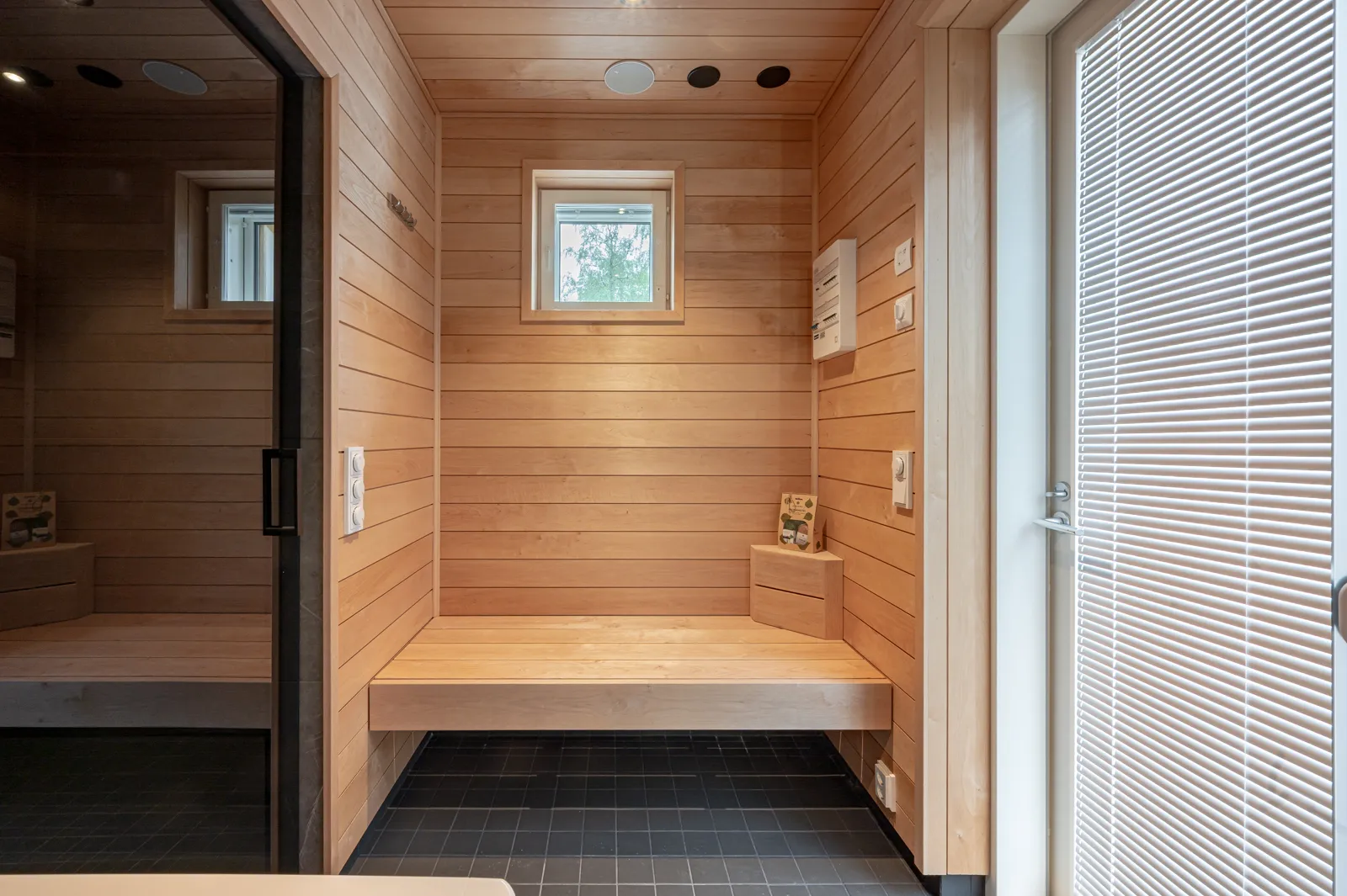Sauna, jossa on puupanelointi, penkki, pieni ikkuna ja valkoiset sälekaihtimet.
