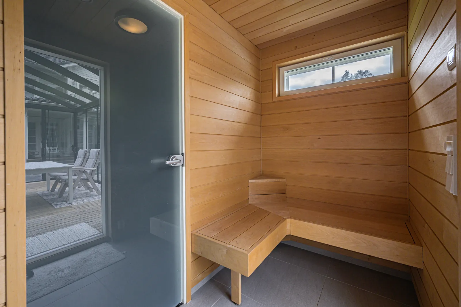 Puinen sauna, jossa on lasiovi ja penkki. Valoisa huone, jossa on ikkuna.