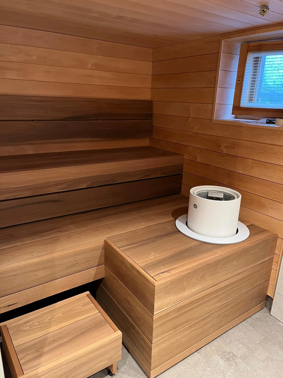 Puinen sauna, jossa on penkit, ikkuna ja valkoinen kiuas.