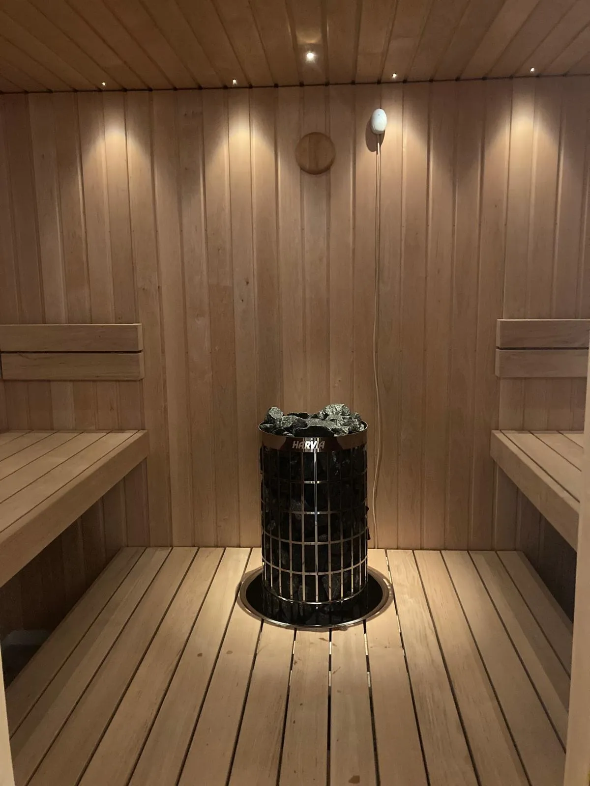 Sauna, jossa on puupanelointi, penkit ja kiuas kivillä. Valoisa ja lämmin tunnelma.