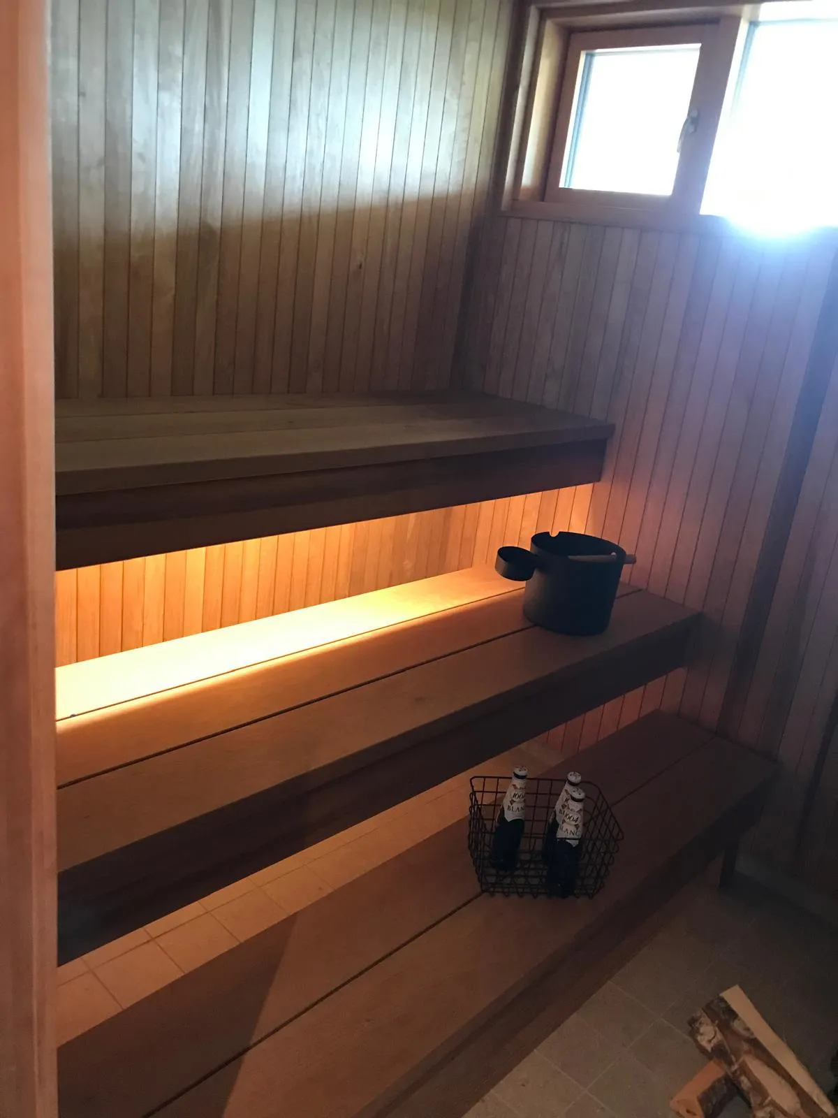 Saunan sisätiloissa on puupaneelit, penkit, kiulu ja juomakori, valaistus on lämmin.