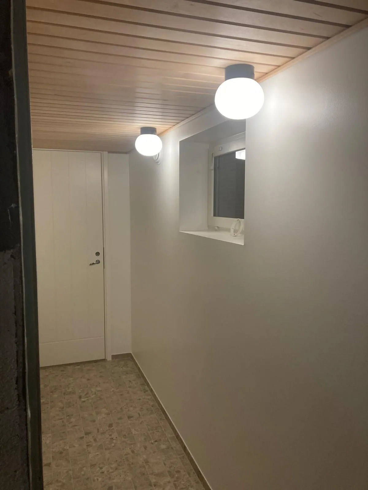 Sisätiloissa on valkoinen ovi, ikkuna ja kaksi pallomaista valaisinta puupaneloidussa katossa.