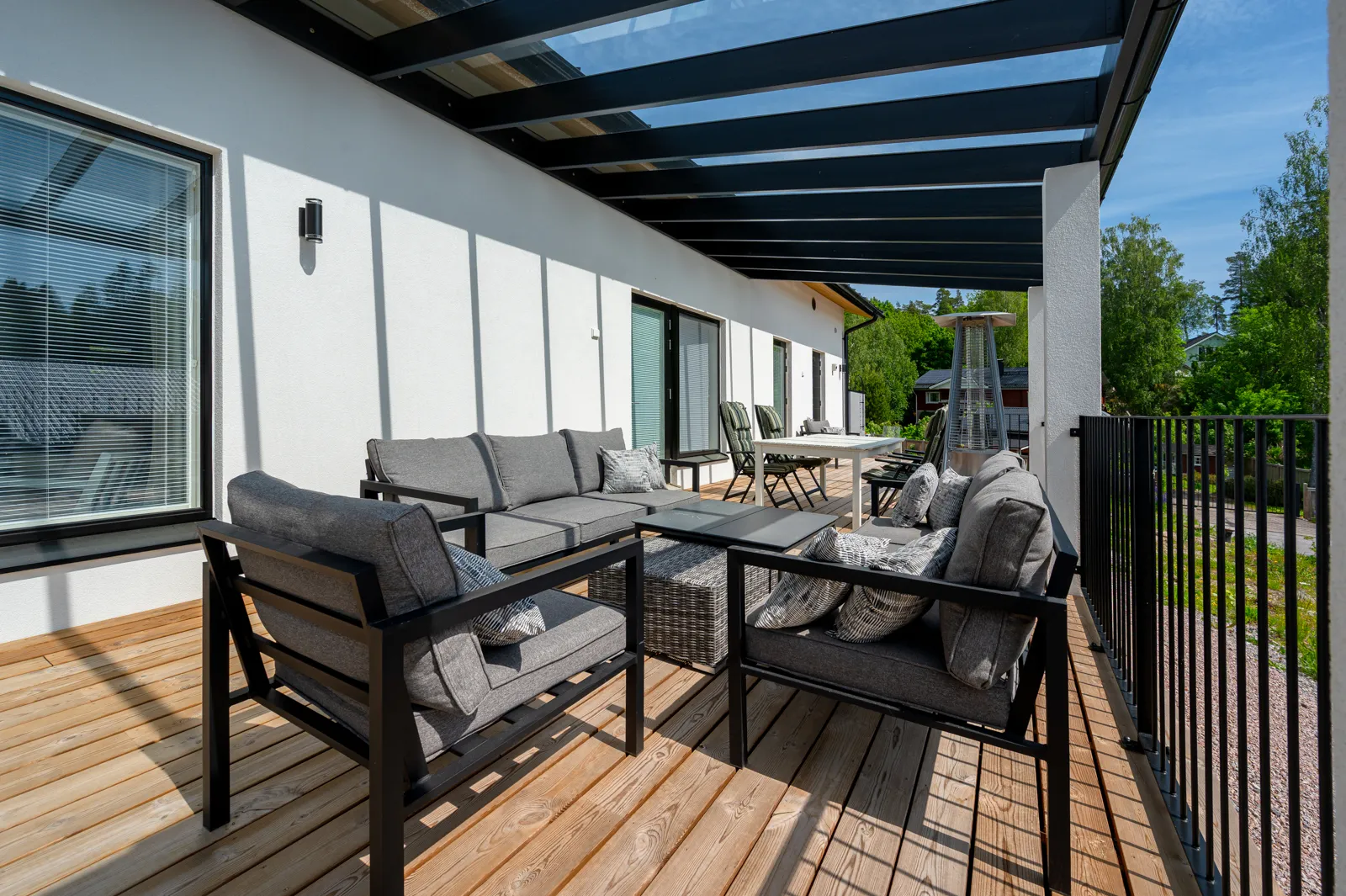 Ulkoterassi harmailla huonekaluilla, puulattialla ja mustalla katoksella, valoisa ja moderni.