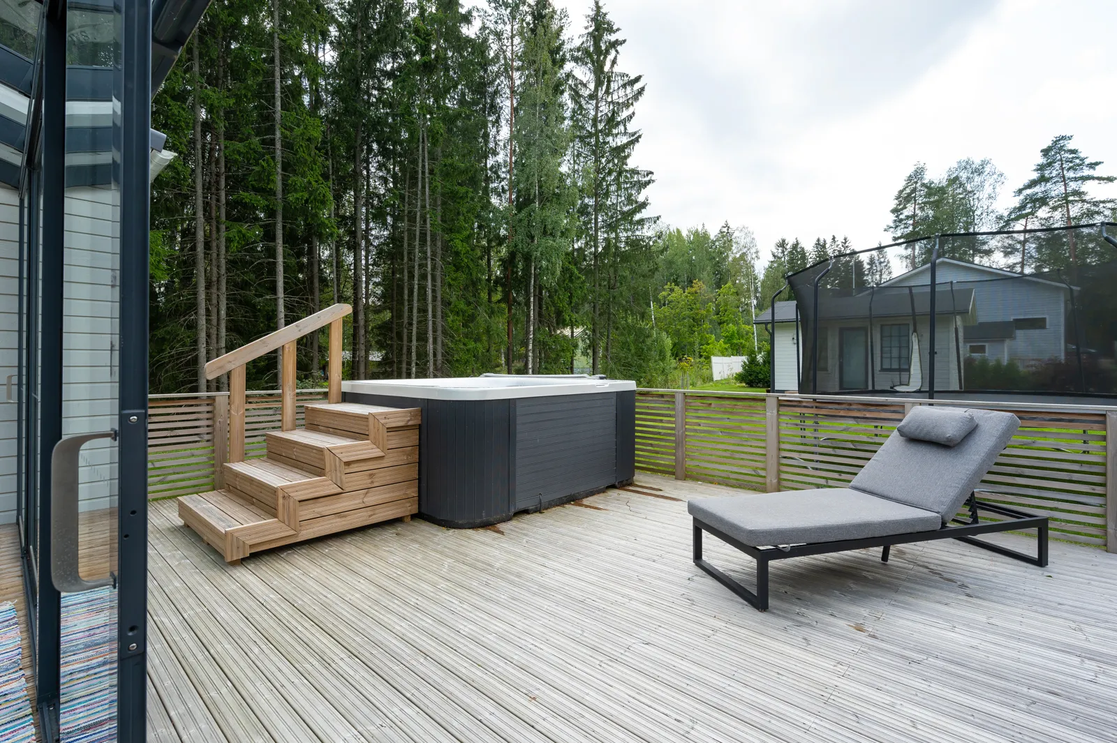 Ulkoterassi, jossa on poreallas, puuportaat, lepotuoli ja taustalla metsä sekä talo trampoliinilla.