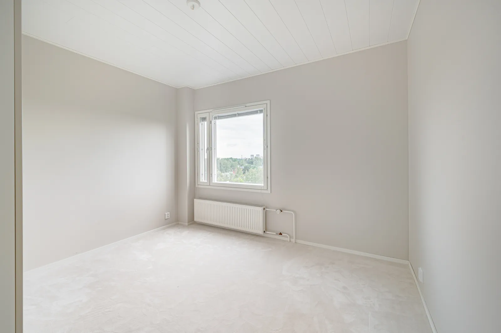 Vaalea, tyhjä huone, jossa on ikkuna, patteri ja valkoinen katto.