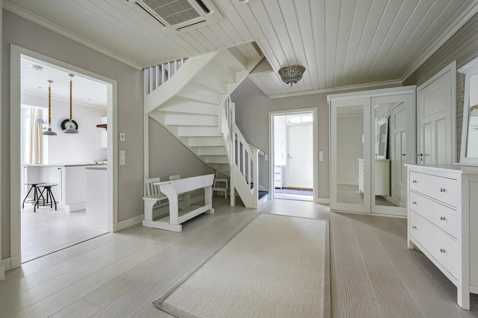 Vaalean eteisen sisustus valkoisella portaikolla, matolla ja huonekaluilla.