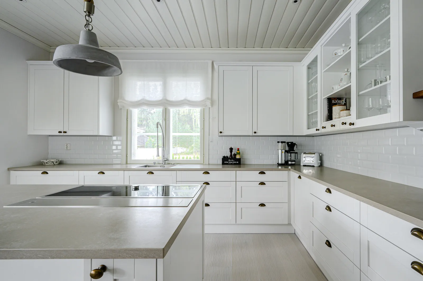 Vaalea keittiö, jossa valkoiset kaapit, harmaa työtaso ja kattovalaisin.