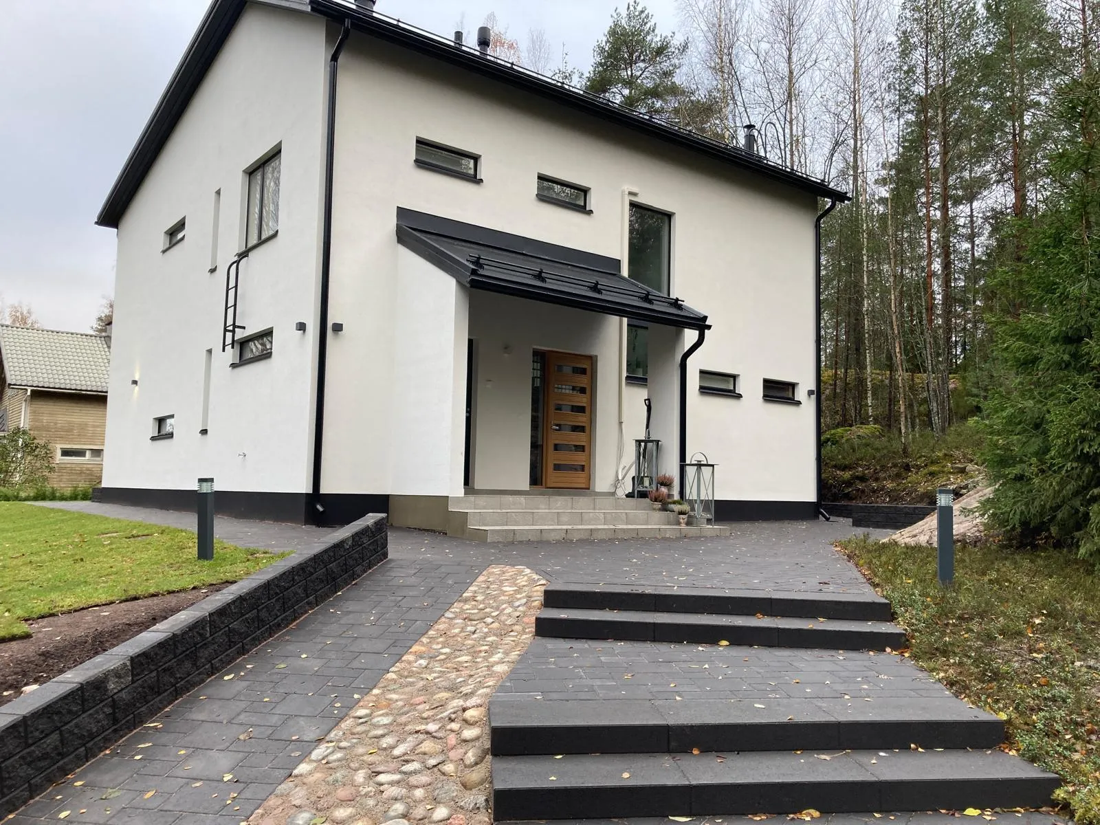 Moderni, valkoinen omakotitalo, jossa on mustat yksityiskohdat, kivetty piha ja luonnonvaloa.