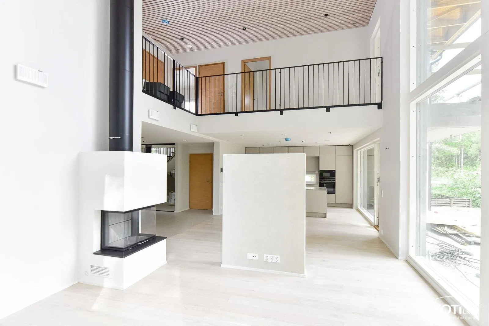 Vaalea, avara sisätila, jossa on takka, parvi ja suuret ikkunat, luoden modernin ja valoisan tunnelman.