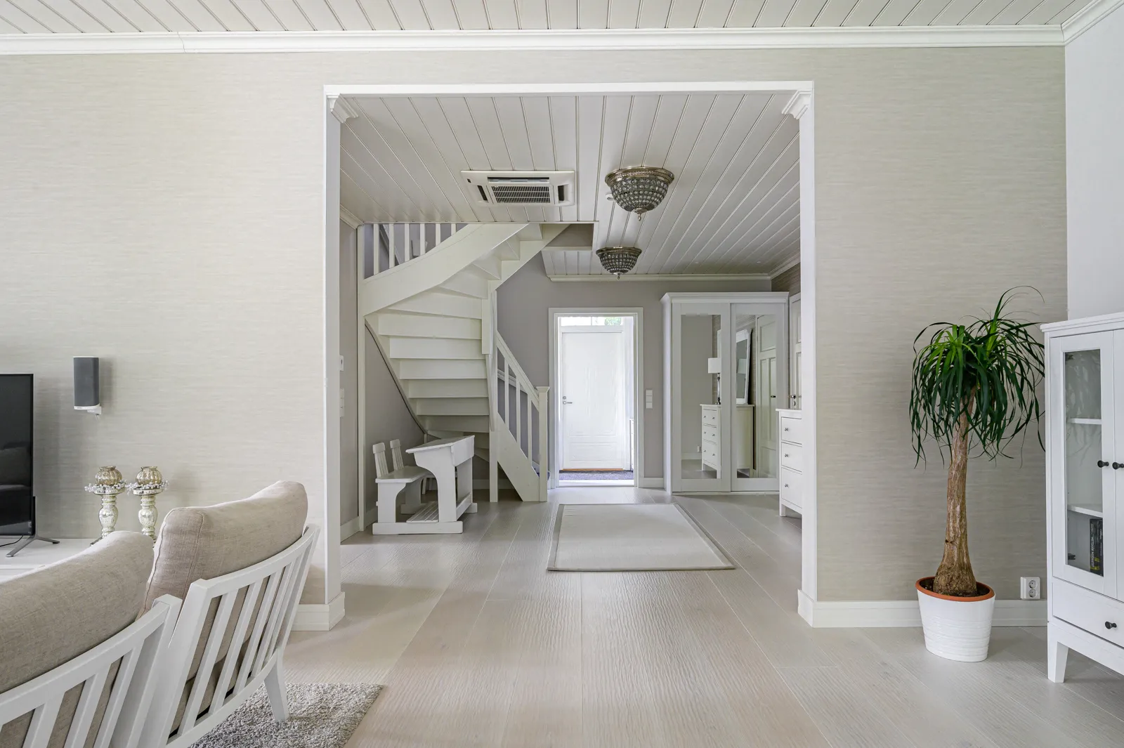 Vaaleassa huoneessa on valkoinen portaikko, valaisimet, viherkasvi ja valoisa tunnelma.